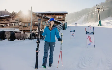 Skisaison-Eröffnungstage Frau in Skikleidung mit Skiern vor Chalet im sonnigen Skigebiet